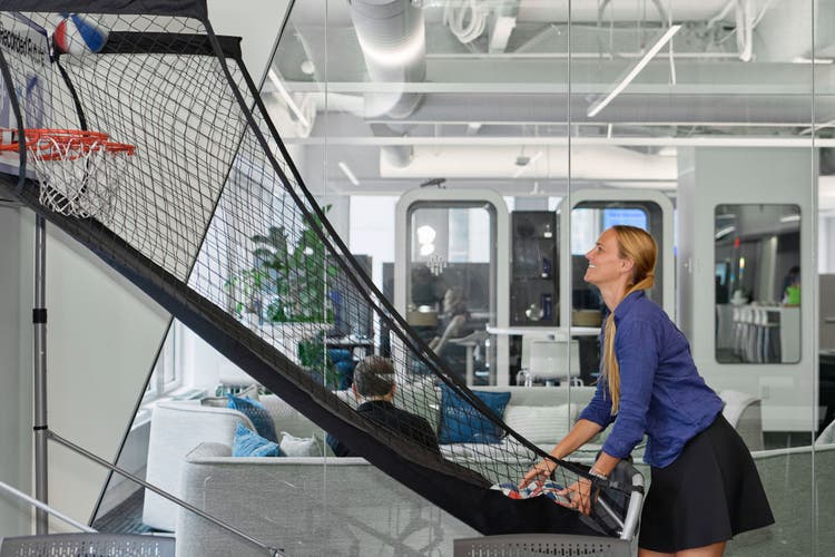 A woman playing arcade basketball in the office.