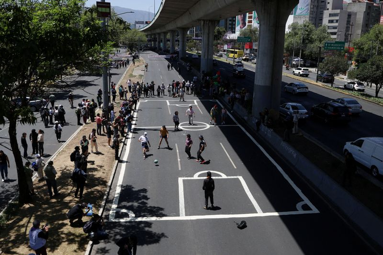 Des manifestants se tiennent debout et des gens jouent au football sur un terrain peint sur l'autoroute.