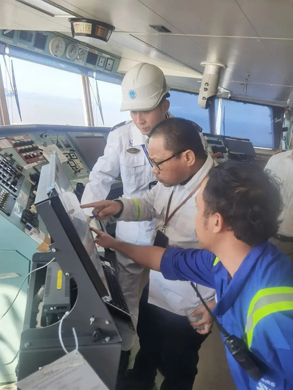 Officials on a bridge of a ship starring at a computer screen